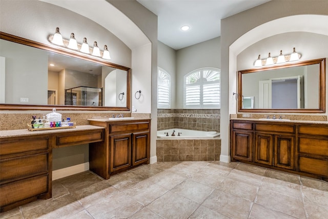 bathroom featuring a shower stall, a bath, two vanities, and a sink