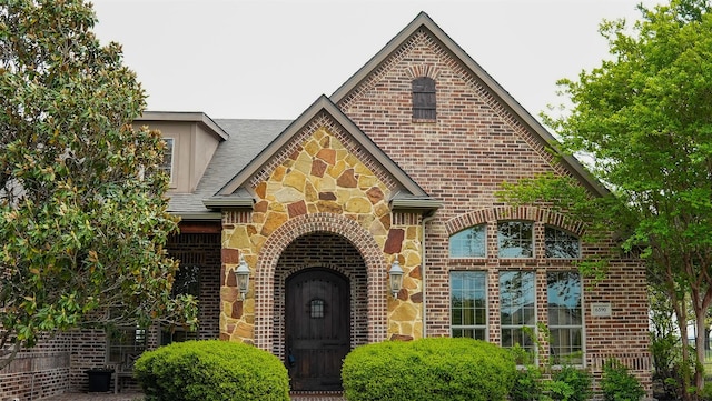 exterior space featuring brick siding, stone siding, and a shingled roof
