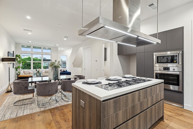 kitchen with appliances with stainless steel finishes, a center island, light wood-type flooring, and range hood