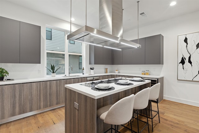 kitchen with a kitchen island, island exhaust hood, sink, a kitchen breakfast bar, and light wood-type flooring