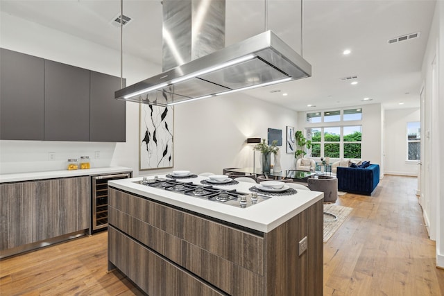 kitchen with a center island, beverage cooler, light hardwood / wood-style flooring, dark brown cabinetry, and island range hood