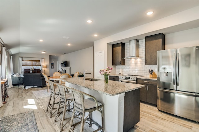 kitchen featuring a center island with sink, stainless steel appliances, a kitchen breakfast bar, wall chimney exhaust hood, and sink