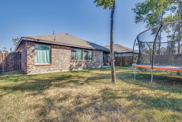 back of house featuring a trampoline and a yard