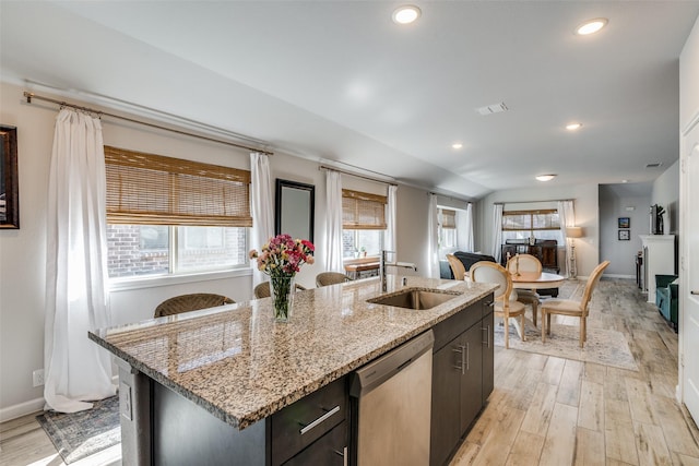 kitchen featuring a center island with sink, light wood-type flooring, vaulted ceiling, stainless steel dishwasher, and sink