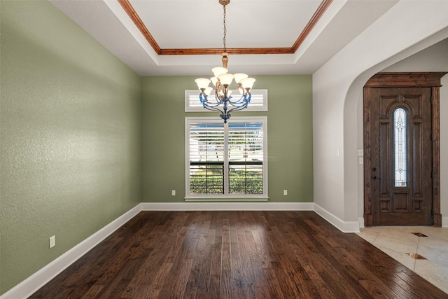 entryway with a notable chandelier, crown molding, wood-type flooring, and a raised ceiling