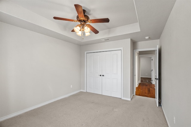 unfurnished bedroom featuring a raised ceiling, light carpet, ceiling fan, and a closet