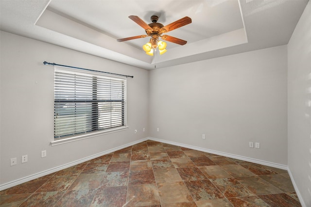 empty room with ceiling fan and a tray ceiling