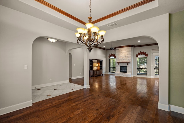 unfurnished living room with crown molding, ceiling fan with notable chandelier, wood-type flooring, a stone fireplace, and a raised ceiling