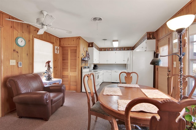 dining room with ceiling fan, wood walls, and light carpet