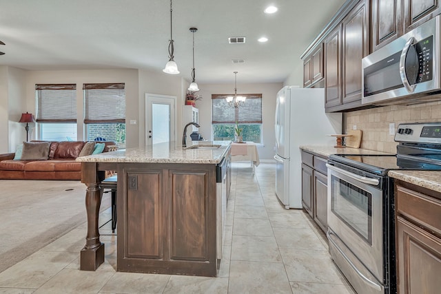 kitchen featuring a notable chandelier, sink, hanging light fixtures, stainless steel appliances, and light stone counters