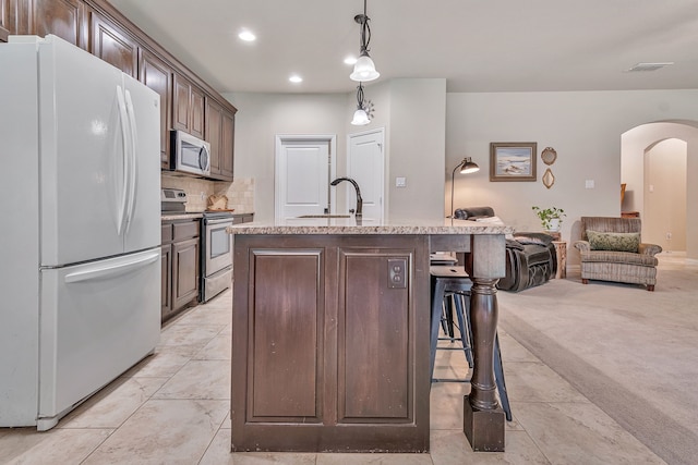 kitchen featuring a center island with sink, pendant lighting, a breakfast bar area, stainless steel appliances, and dark brown cabinets