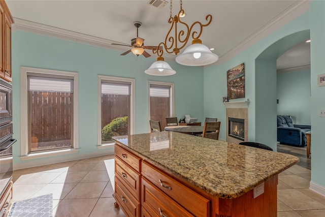 kitchen with a kitchen island, decorative light fixtures, crown molding, a fireplace, and stone counters