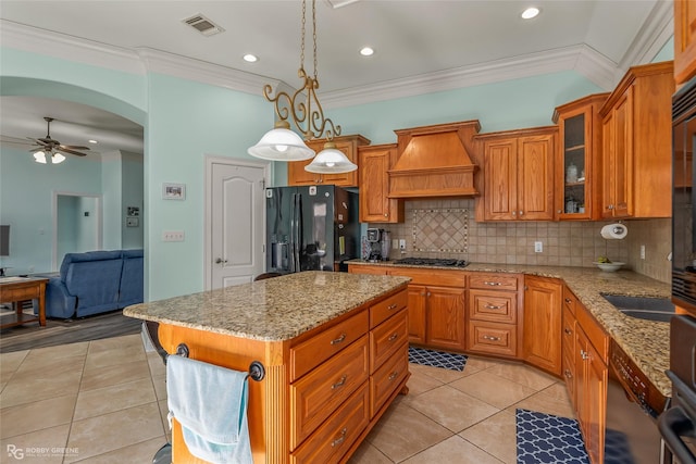 kitchen featuring decorative light fixtures, ceiling fan, a kitchen island, black fridge with ice dispenser, and custom range hood