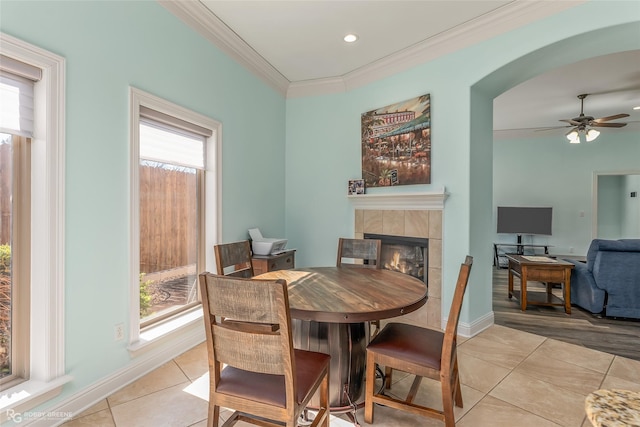 tiled dining room with ceiling fan, a tile fireplace, and ornamental molding