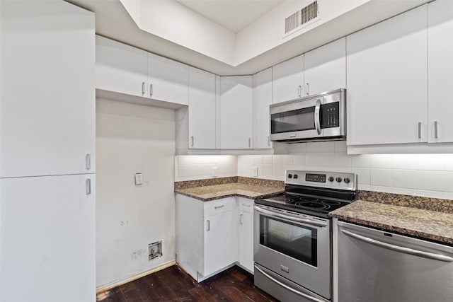 kitchen featuring appliances with stainless steel finishes, white cabinetry, dark hardwood / wood-style flooring, dark stone counters, and backsplash