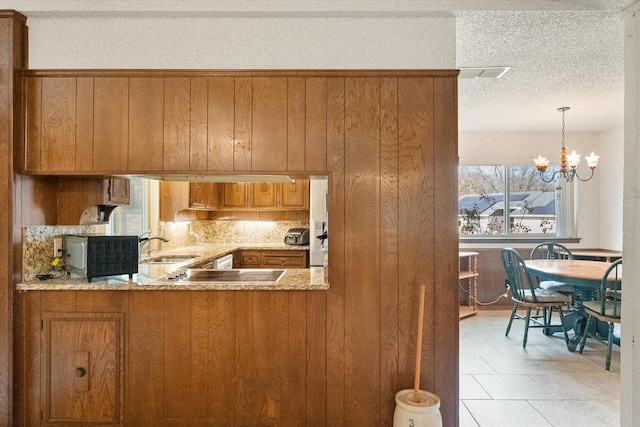 kitchen with light stone counters, brown cabinets, a textured ceiling, a chandelier, and a sink