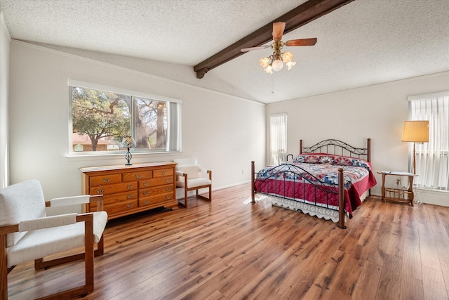 bedroom with a textured ceiling, ceiling fan, hardwood / wood-style flooring, and vaulted ceiling with beams