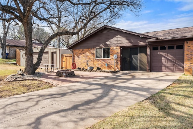 view of front facade featuring an attached garage, driveway, a fire pit, and brick siding