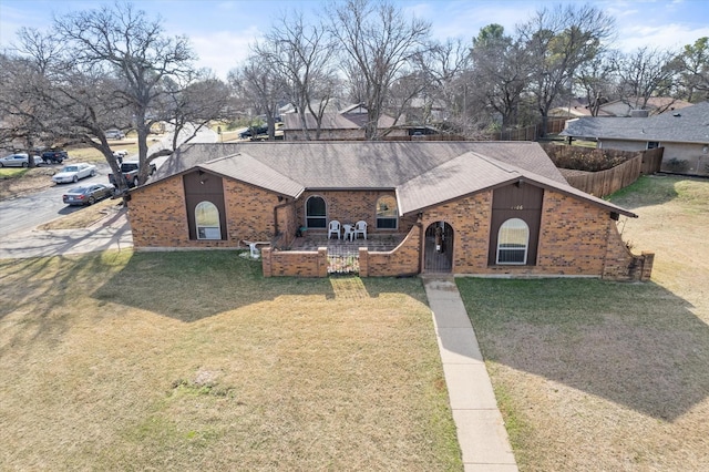 view of front of house featuring brick siding, a front yard, fence, and a shingled roof