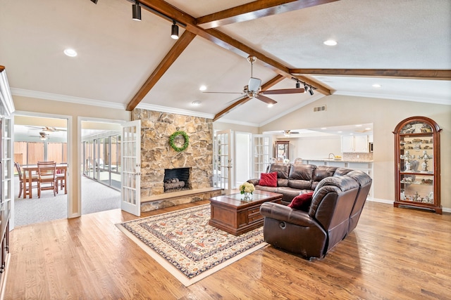 living room with a stone fireplace, ceiling fan, light wood-type flooring, french doors, and lofted ceiling with beams