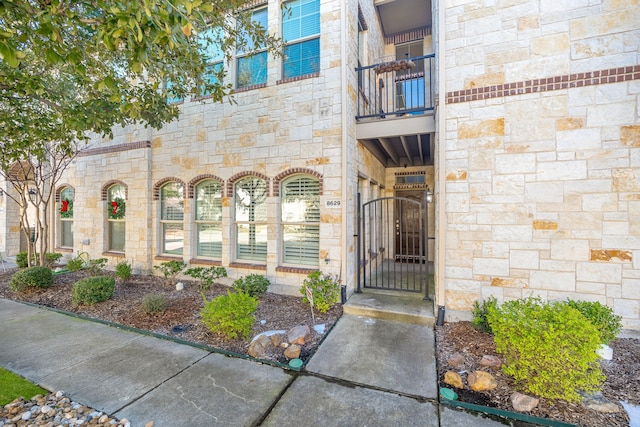 entrance to property featuring a balcony, a gate, and stone siding