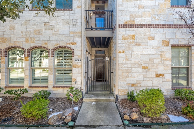 entrance to property featuring stone siding, a balcony, and a gate