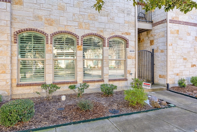 view of exterior entry featuring stone siding, fence, a balcony, and a gate