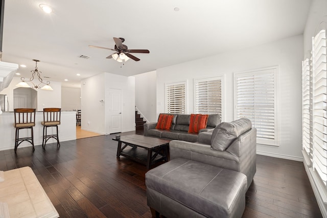 living room with stairs, visible vents, dark wood-type flooring, and a ceiling fan