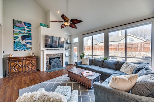 living room with ceiling fan, dark hardwood / wood-style floors, a stone fireplace, and high vaulted ceiling