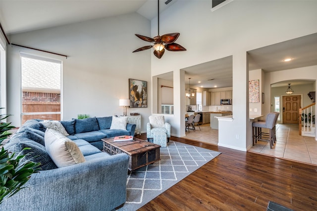 living room with ceiling fan with notable chandelier, hardwood / wood-style floors, and high vaulted ceiling