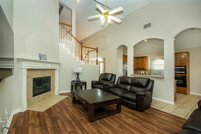 living room featuring high vaulted ceiling, dark wood-type flooring, a tiled fireplace, and ceiling fan