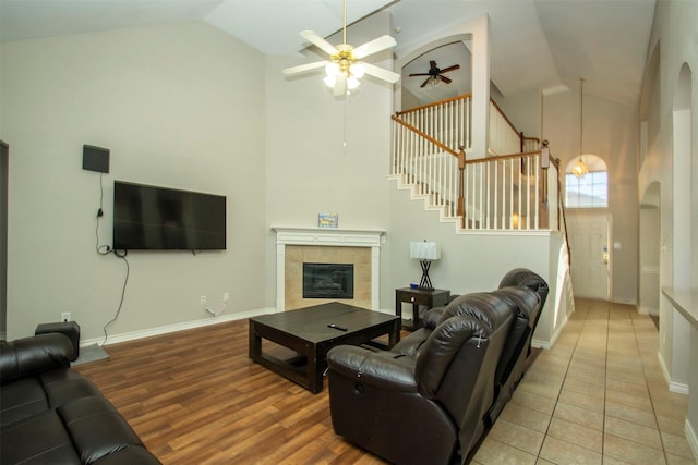 living room featuring ceiling fan, a tiled fireplace, light hardwood / wood-style flooring, and high vaulted ceiling