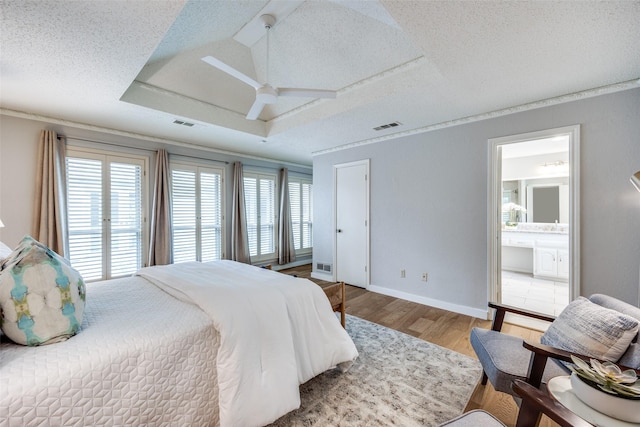 bedroom featuring ensuite bathroom, a textured ceiling, light wood-type flooring, a raised ceiling, and access to exterior