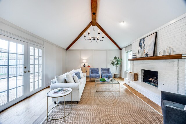 living room with french doors, lofted ceiling with beams, a brick fireplace, a notable chandelier, and light hardwood / wood-style floors