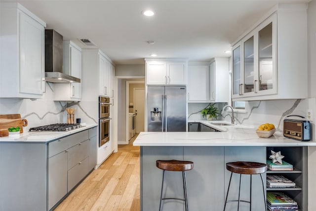 kitchen with wall chimney range hood, stainless steel appliances, sink, and white cabinets