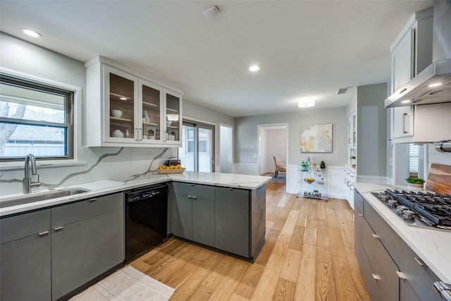 kitchen featuring sink, black dishwasher, white cabinets, light stone counters, and wall chimney range hood