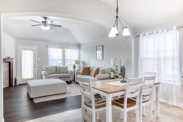 tiled dining space featuring ceiling fan with notable chandelier and vaulted ceiling