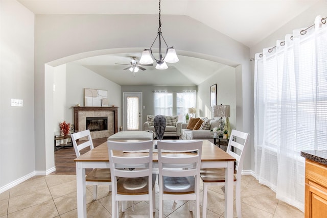 dining area featuring vaulted ceiling, light tile patterned flooring, ceiling fan with notable chandelier, and a tiled fireplace