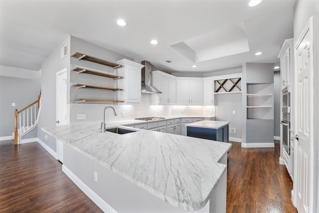 kitchen with wall chimney exhaust hood, sink, white cabinetry, kitchen peninsula, and a kitchen island