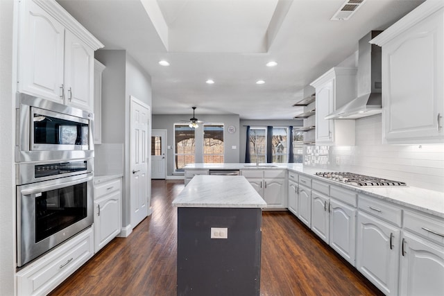 kitchen with stainless steel appliances, white cabinetry, and wall chimney exhaust hood