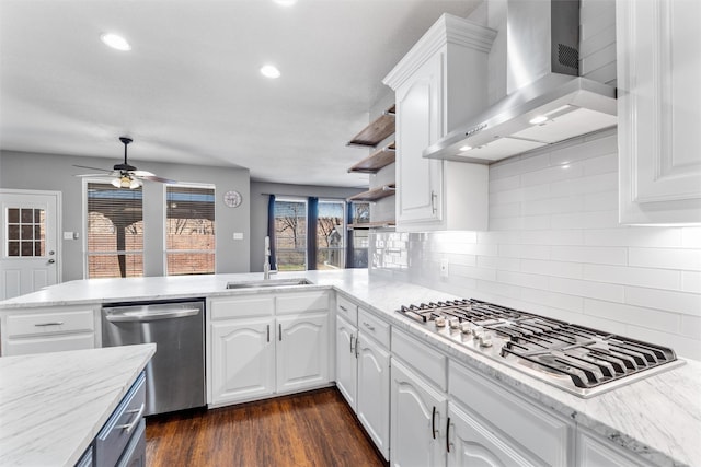 kitchen featuring white cabinets, kitchen peninsula, wall chimney exhaust hood, and appliances with stainless steel finishes