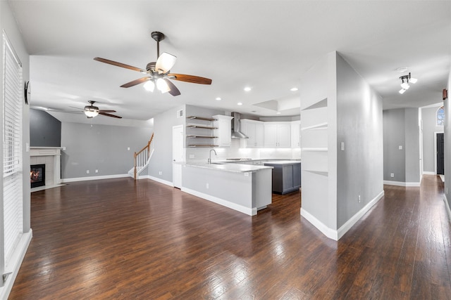 kitchen featuring white cabinetry, dark hardwood / wood-style floors, kitchen peninsula, a tiled fireplace, and wall chimney range hood