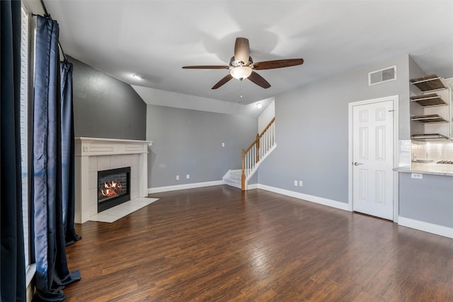 unfurnished living room with a tiled fireplace, vaulted ceiling, dark hardwood / wood-style floors, and ceiling fan