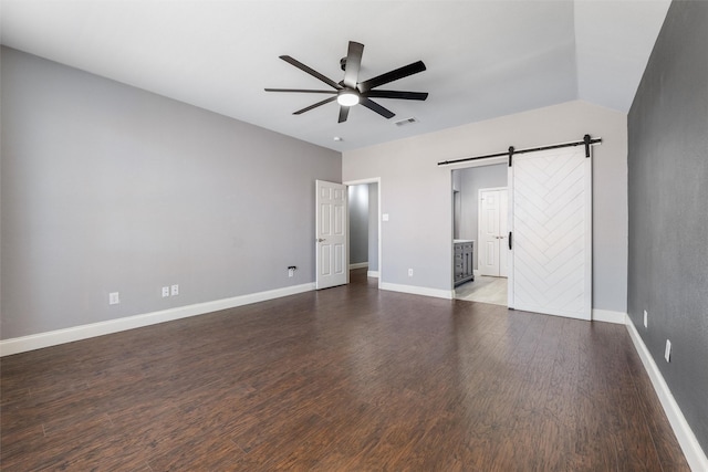 unfurnished bedroom with ceiling fan, connected bathroom, a barn door, and dark hardwood / wood-style flooring