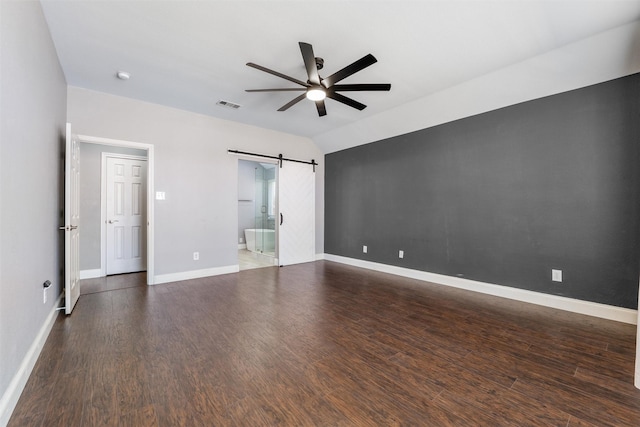 spare room featuring vaulted ceiling, a barn door, dark hardwood / wood-style floors, and ceiling fan