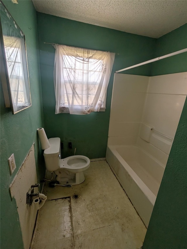 bathroom with toilet, a textured ceiling, a healthy amount of sunlight, and washtub / shower combination