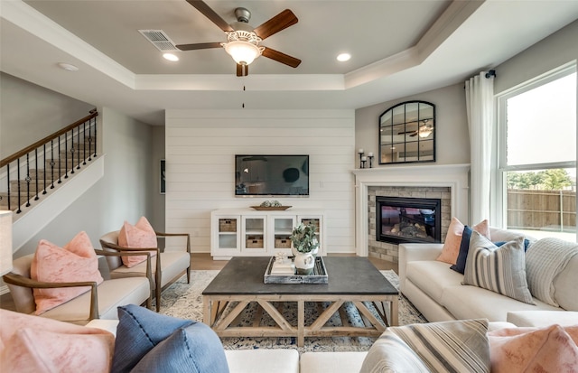 living room featuring ceiling fan, hardwood / wood-style floors, a tray ceiling, and a tiled fireplace