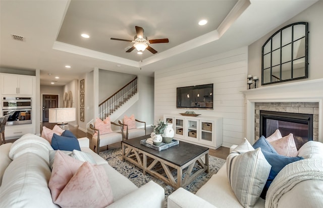 living room with ceiling fan, a fireplace, wood-type flooring, and a tray ceiling