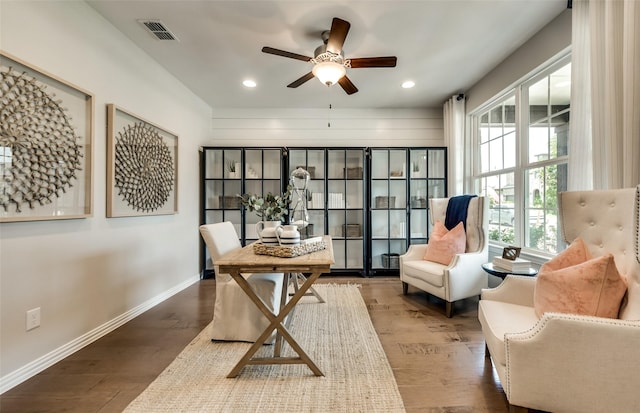 living area with ceiling fan, dark wood-type flooring, and wooden walls