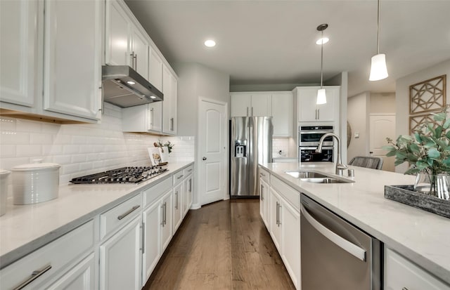 kitchen with wall chimney range hood, sink, hanging light fixtures, appliances with stainless steel finishes, and white cabinets